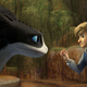 A young boy in a hoodie approaches a black-and-white Night Fury dragon.